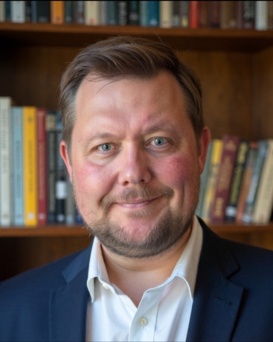 Kennon Bauman, founder of Quest Coaching Services, in a navy jacket in front of a bookshelf